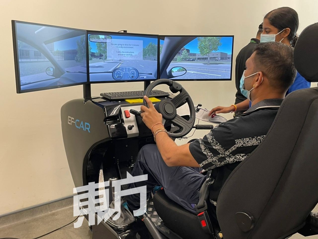 一名患者在治疗师的陪同下，使用驾驶模拟器练习驾驶技术。