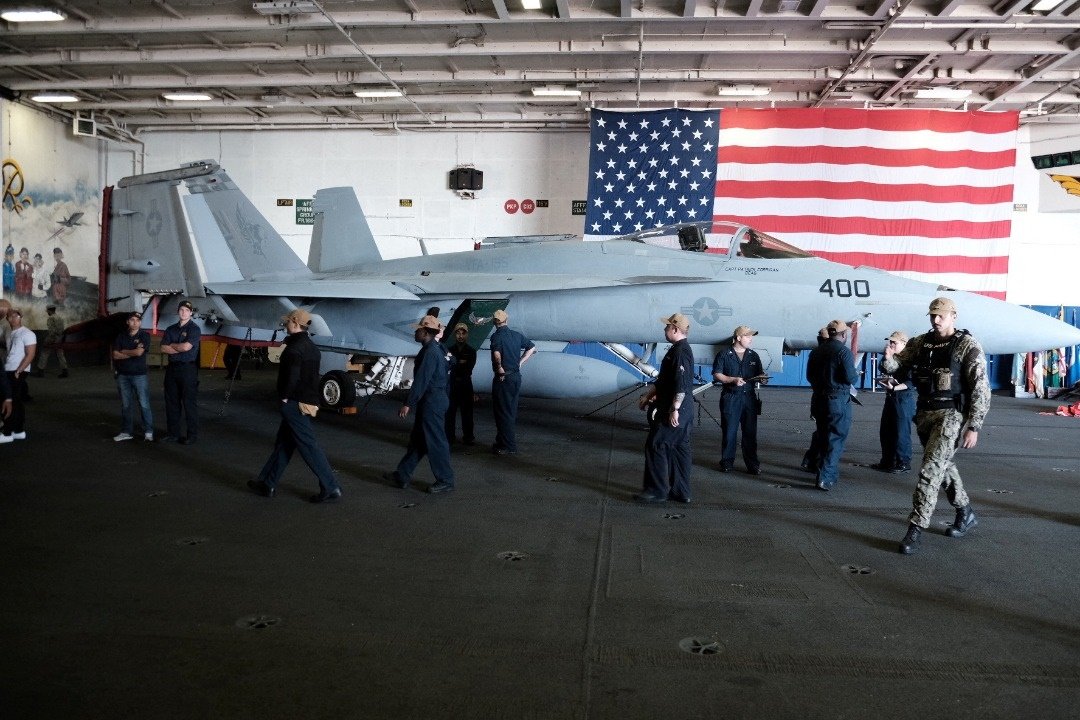 在“里根”号航空母舰的机库甲板上，机组人员走过一架F/A-18超级大黄蜂战斗机。（图取自路透社）